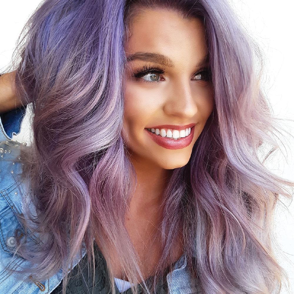 Woman with wavy purple hair smiling against a white background