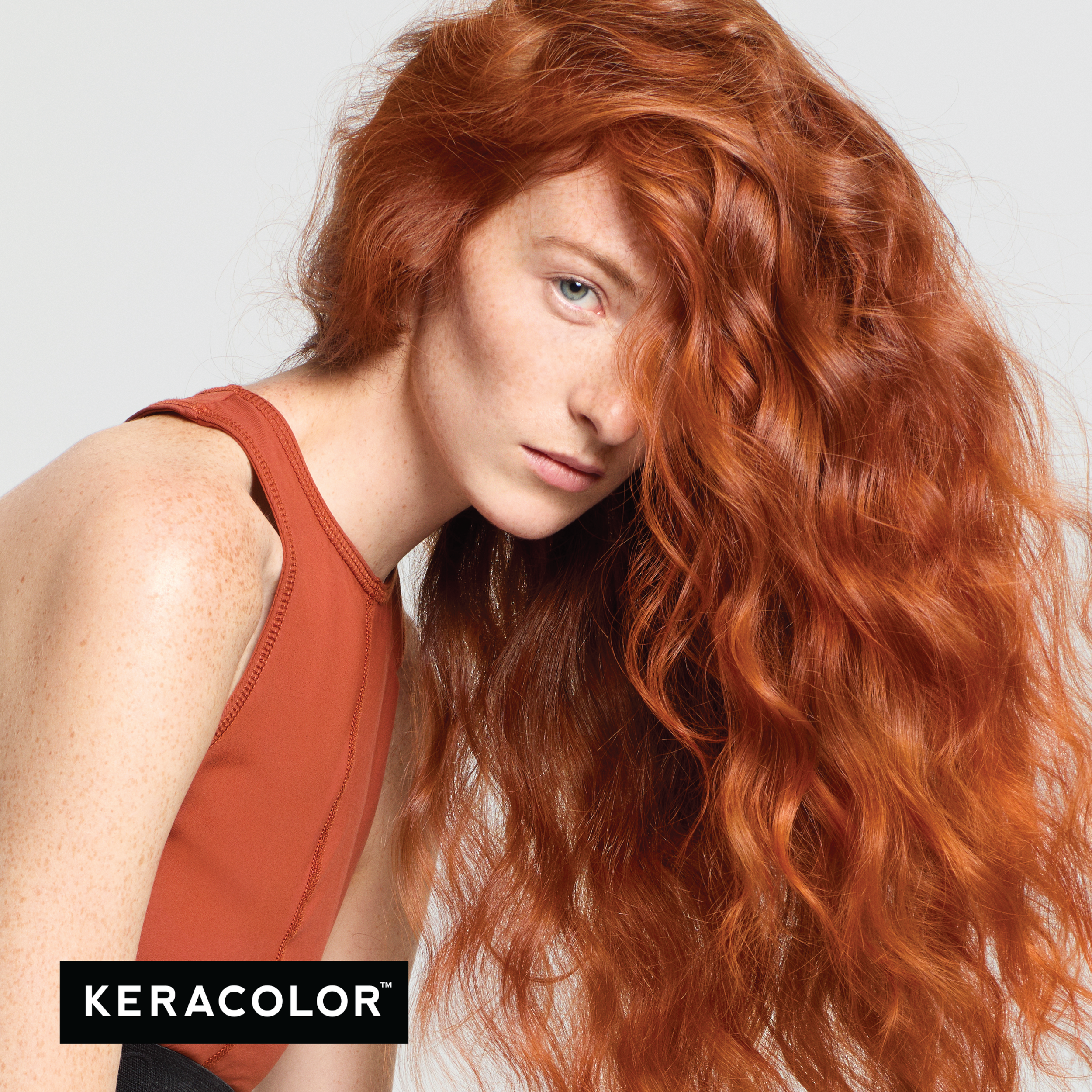 Person with long, wavy red hair wearing a rust-colored sleeveless top on a light gray background, with Keracolor logo.
