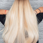 Close-up of a person with long, straight blonde hair against a gray background