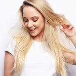 Woman with long blonde hair touching it against a white background